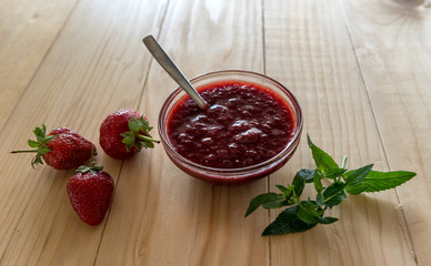 Homemade strawberry jam in a a glass bowl with fresh ripe strawberries on a wooden table