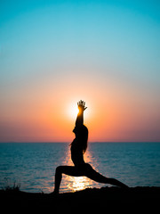 Young slim girl practicing yoga on mountain against ocean or sea at sunrise time. Silhouette of...