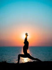 Schilderijen op glas Young slim girl practicing yoga on mountain against ocean or sea at sunrise time. Silhouette of woman in rays of awesome sunset. © kohanova1991