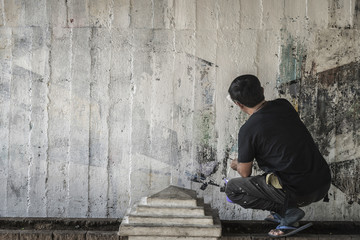 Young man clean the walls by painting white over the old cement wall.