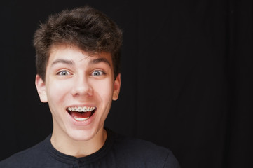A funny teen on a black background laughs with wide open eyes and mouth. Braces on his teeth are clearly visible