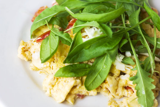 Egg omelet with tomato and fresh arugula spinach in white plate