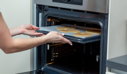 Woman put raw dough in oven in kitchen closeup.