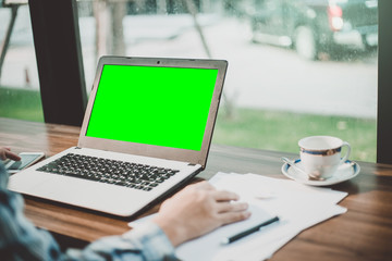 Close-up of businessman working with mockup image of laptop with blank green screen and smartphone...