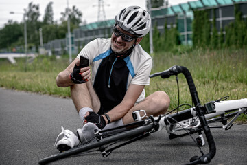 Naklejka premium Injured biker holding his smartphone calling rescue team