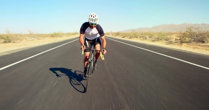 Young healthy man cycling on road bike outside on desert road on sunny day with blue sky in background 
