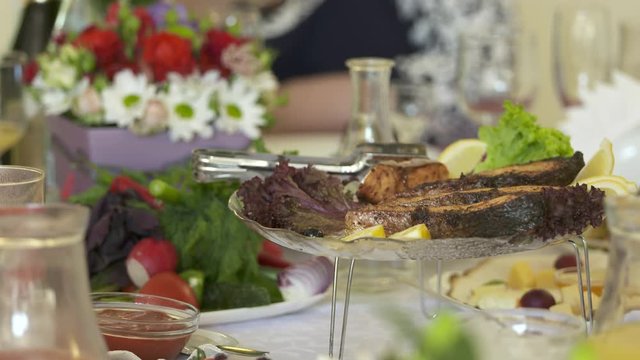 People celebrate holidays at festive dinner. Close-up of dining table with appetizers beverages and grilled salmon steaks on decorative platter.