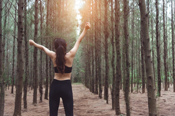 Fototapeta premium Women stretching arms and breathing fresh air in middle of pinewood forest while exercising. Workouts and Lifestyles concept. Happy life and Healthcare theme. Nature and Outdoors theme. Back view