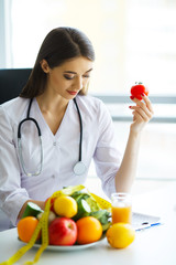 Health. Health Dietitian Sits At A Table With Fruits And Vegetables. The Doctor Draws up a Nutrition Plan. The Doctor Smiles at Vibrating Happy and Holds in the Tomatoes Hands.High Resolution