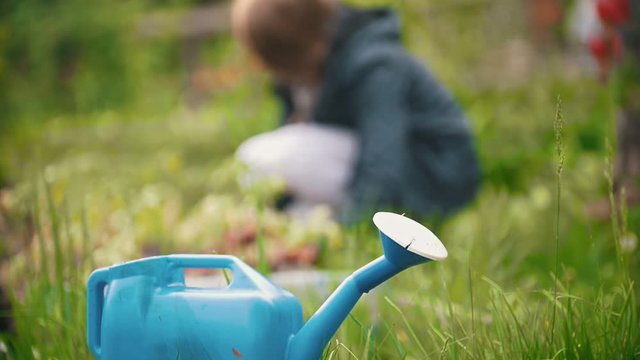 Blue watering can, in the background a girl sitting digs up the earth