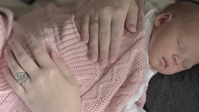 Loving mum stroking newborn baby daughter covered in pink blanket and sleeping on her chest. Mother and child bonding