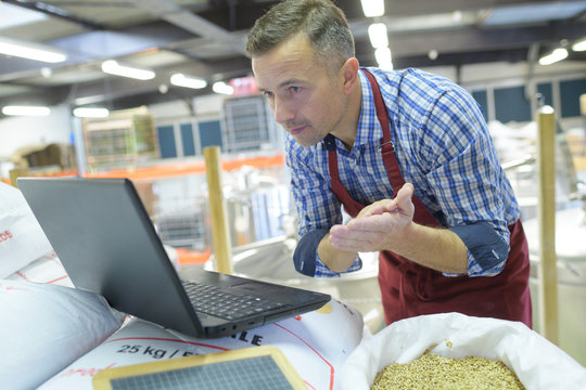 Man looking at laptop balanced on sacks of grain