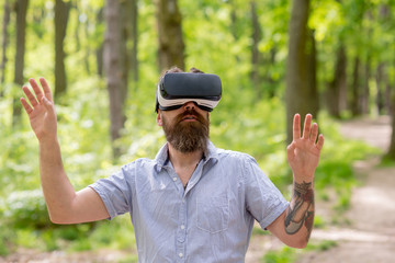 Bearded man enjoying 360 degree perspective in VR glasses. Excited man with modern device roaming in woods. Era of virtual world, technology concept