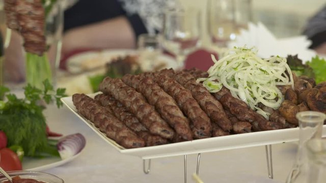 Dinner table served with lula kebabs and fresh vegetables. People enjoy Armenian style kebab at restaurant.
