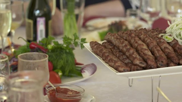 Dinner table served with lula kebabs and fresh vegetables. People enjoy Armenian style kebab at restaurant.
