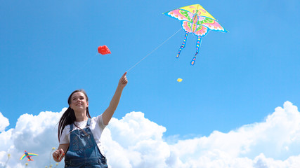 A, young, pregnant, girl, jumpsuit, launches, kite, against, blue, sky, clouds.