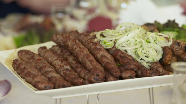 Dinner table served with lula kebabs and fresh vegetables. People enjoy Armenian style kebab at restaurant.