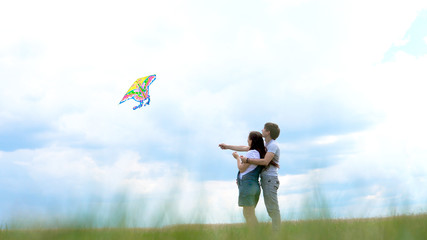 Young family, couple running a kite against a blue sky and clouds