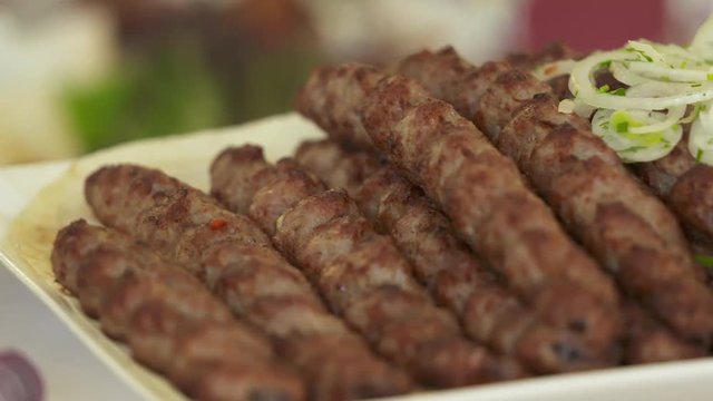 Dinner table served with lula kebabs and fresh vegetables. People enjoy Armenian style kebab at restaurant.