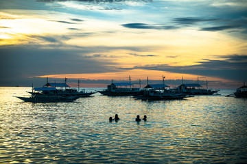 Obraz premium Swimming Tourists and Tour Boats in the Sea at Sunset