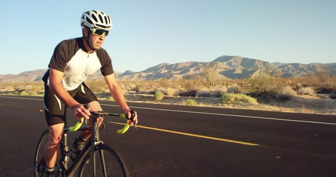 Young man cycling on road bike outside on desert road on sunny day