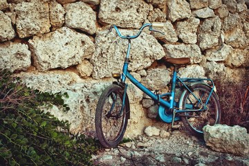 Old blue vintage bicycle leaning against a stone wall in the sun in the Mediterranean