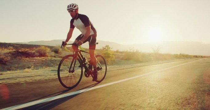 Young man cycling on road bike outside on desert road at sunset with lens flare 