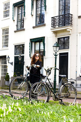 Fototapeta premium Woman girl parking vintage bicycle street old town sity black coat long curly hair enjoy sun spring glasses white house
