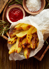 Baked potato fries, wedges with addition sea salt and rosemary on a wooden background, top view. Tasty snack