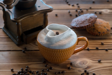 Cup of coffee with foam in the form of a heart with cookies and coffee beans with coffee grinder on a wooden table