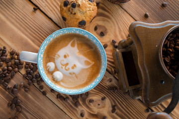 Cat foam face of latte art coffee in cup with scattered coffee beans and biscuits on old wooden table