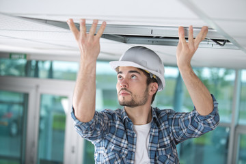 man in builder uniform hand up installing suspended ceiling - obrazy, fototapety, plakaty