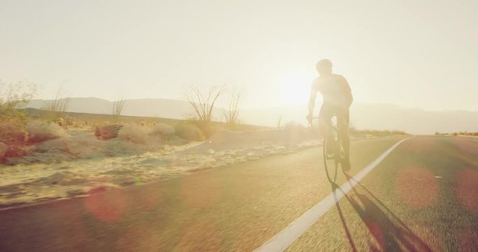 Young man cycling on road bike outside on desert road at sunset with lens flare 