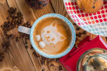 Red coffee mill, cup latte with a painted cat on milk foam and biscuits on a old wooden table.