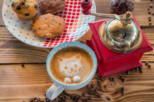 Red coffee mill, cup latte with a painted cat on milk foam and biscuits on a old wooden table.