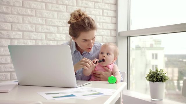 Working mom with child on table. Business woman with baby working on laptop. Working together with kid. Businesswoman holding toddler girl on hand. Female home work. Woman freelancer at cozy home