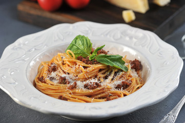 Spaghetti with bolognese sauce in a white deep dish. The pasta is decorated with basil and sprinkled with Parmesan cheese. Close-up. Macro photography.