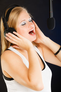Woman singing to microphone wearing headphones in studio
