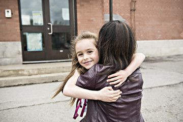 Fototapeta premium A girl child and his mother hugging outside at school