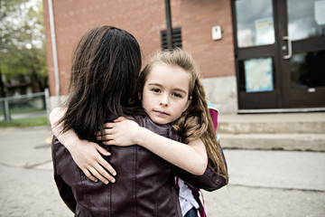 A girl child and his mother hugging outside at school