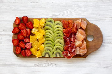 Chopped fruits arranged on cutting board on white wooden background, top view. Ingredients for fruit salad. From above, flat, overhead.