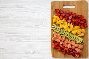 Chopped fresh colorful fruits arranged on cutting board on white wooden background, top view. Copy space and text area. Flat lay. From above.