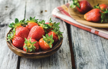 Fresh strawberries in a wooden bowl on a rustic wooden table