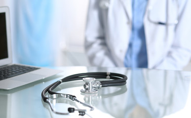 Stethoscope lying on glass desk with laptop computer at busy physician background. Medicine or pharmacy concept. Medical tools at doctor working table