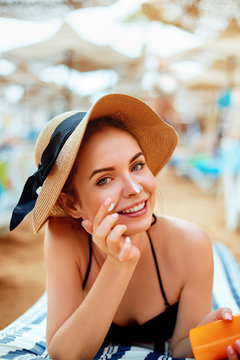 Suntan   woman in hat applying sunscreen solar. Beautiful happy woman smear  lotion  with sun cream   to her nose. Skincare.
