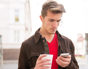 Casual man with coffee watching phone sadly