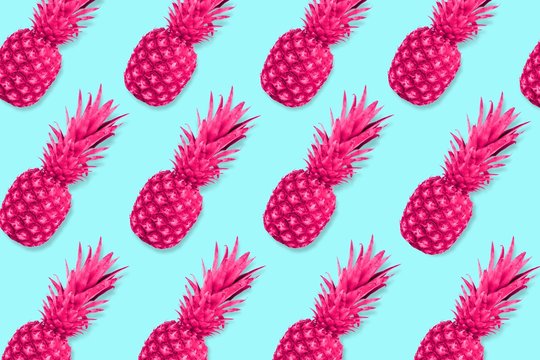 Colorful fruit pattern, Neon pink pineapples on a pastel blue background. Top view.