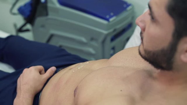 A close-up of how the doctor applies the gel on the patient's stomach and leads the abdomen with a device for radiofrequency lifting. The cosmetologist conducts the RF-lifting procedure for a man.