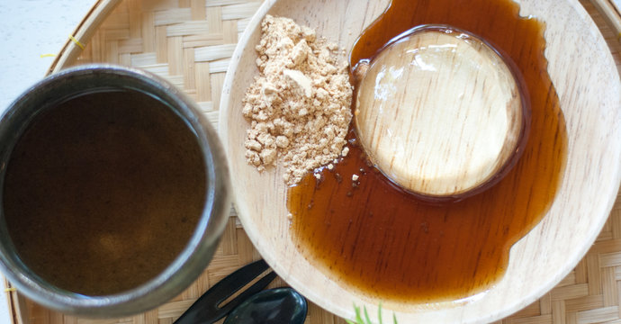 Japanese transparent mochi on wooden plate with sweet sauce, sugar and tea mug taken from top view