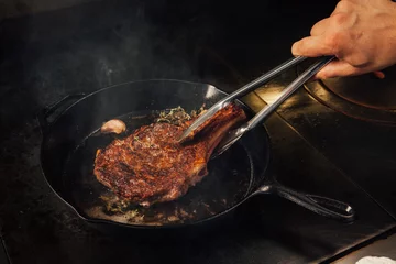 Gartenposter Steak in einer gusseisernen Pfanne kochen. © Thoffman